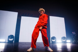 Australian-American singer Betty Who performs on stage in a red suit and sunglasses, holding a microphone