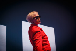 Australian-American singer Betty Who performs on stage in a red suit and sunglasses, holding a microphone