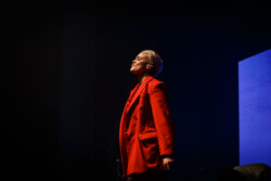 Australian-American singer Betty Who performs on stage in a red suit holding a microphone