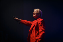 Australian-American singer Betty Who performs on stage in a red suit holding a microphone out to the crowd