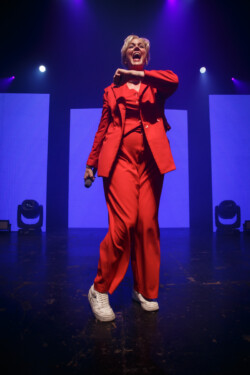 Australian-American singer Betty Who performs on stage in a red suit holding a microphone
