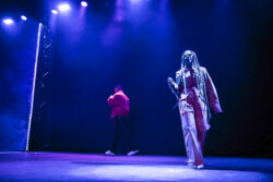 Valie of of Emotional Oranges performing in an orange jumpsuit, sunglasses and long braids