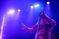 Valie of of Emotional Oranges performing in an orange jumpsuit, sunglasses and long braids