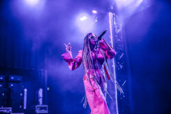Valie of of Emotional Oranges performing in an orange jumpsuit, sunglasses and long braids